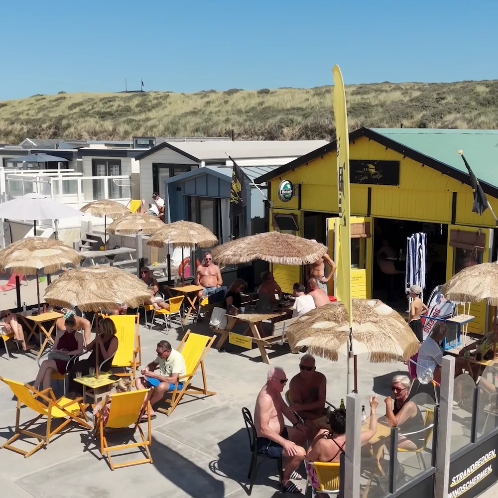 Het terras met rieten parasols en gasten in gele strandstoelen